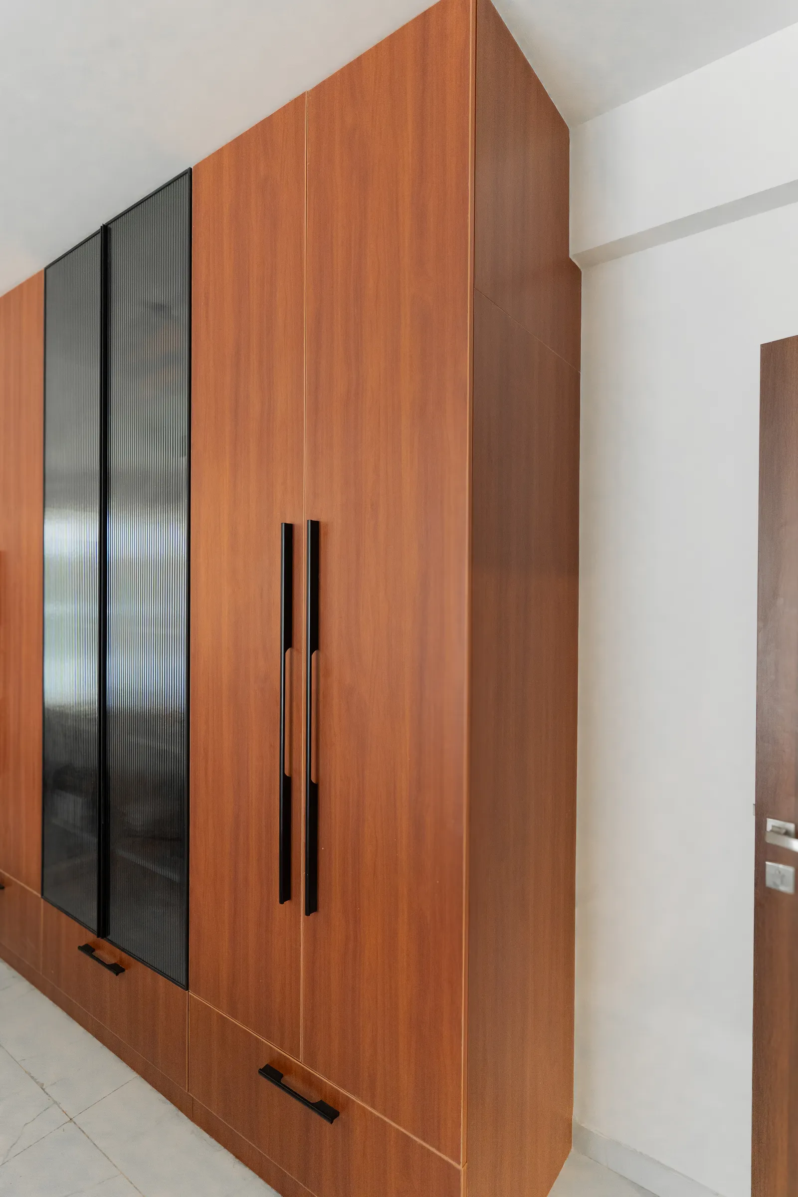 Tall teak-finish wardrobe with tinted glass panel — Karthik's Residence